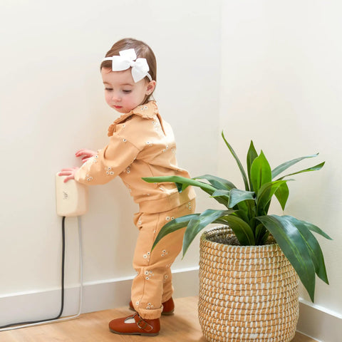 Child near outlet cover with cord shortener for baby proofing provides full outlet coverage keeps excess cords off the floor stores up to four feet of cords kid safe and easy to remove totally great for curious little ones in corner next to plant