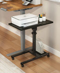 Black mobile adjustable height laptop desk on wheels, swiveling beside a main desk, with printer on 15 by 12 inch surface.