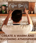 Person hanging a Cozy Coffee Bar Wall Sign For Kitchen And Cafe Decor Vintage Farmhouse Cafe Sign Small Countertop Coffee Station Wall Art Rustic Coffee Decor For Home Kitchen Perfect Gift in a cozy café setting.