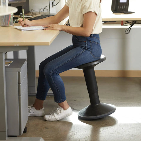 Person seated on SitWell Wobble Stool With Adjustable Height For Active Seating In Classrooms And Libraries, black stool.