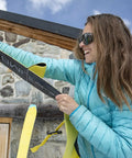 Person attaching Climb 2.0 Ready Climbing Skin for Backcountry Touring And Ski Mountaineering, 140mm Wide, Medium, outside a cabin