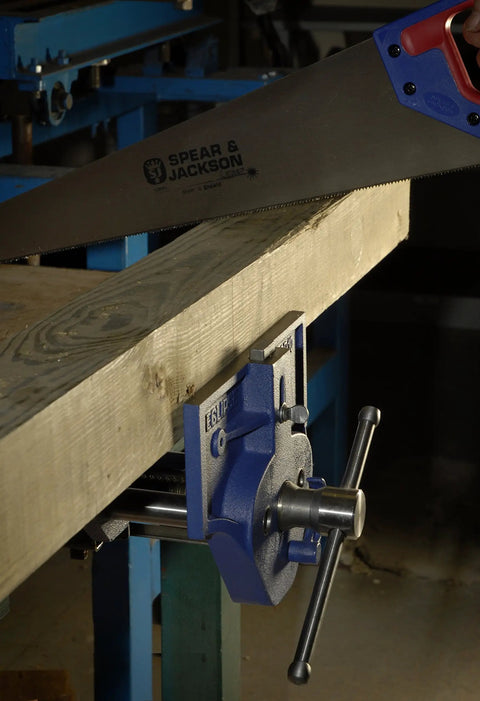 Beefy 7 Inch Quick Release Woodworking Vise with heavy duty cast iron body securing wood for sawing in a workshop setting