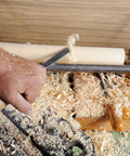 Woodturning lathe in operation with a metal chisel shaping a wooden spindle; wood shavings all around.