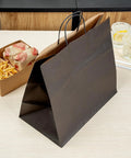 100 Pack Stand Open Paper Shopping Bags With Handles For Grab And Go Takeout And Retail Durable Kraft Paper Carrier Bags 14.17 X 8.26 X 13.19 Inches Easy Carry Totes For Gifts Groceries And Everyday Shop Runs on a table next to food items.