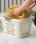 Person placing blanket into 30L Plastic Laundry Hamper With Built In Comfort Carry Handles 2 Pack Nestable Ventilated Clothes Basket