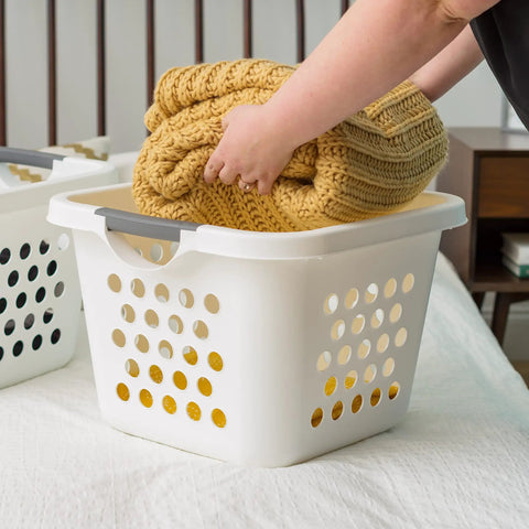 Person placing blanket into 30L Plastic Laundry Hamper With Built In Comfort Carry Handles 2 Pack Nestable Ventilated Clothes Basket