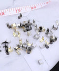 60 Piece Zipper Stopper Kit With Top And Bottom Zipper Stops For Bags Coats And Jackets, bronze and silver stops on marble surface.