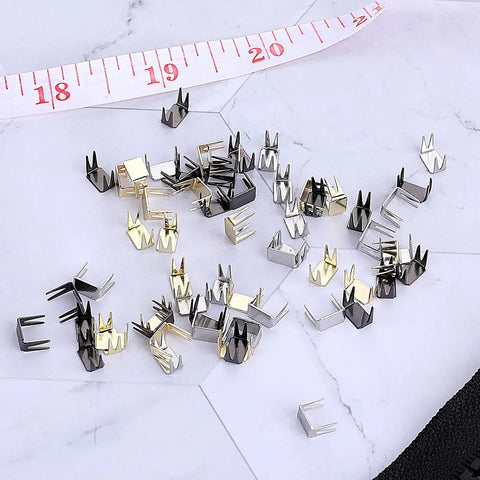 60 Piece Zipper Stopper Kit With Top And Bottom Zipper Stops For Bags Coats And Jackets, bronze and silver stops on marble surface.