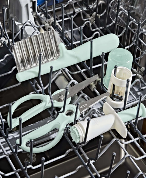 OXO Tot crinkle cutter with mint-green handle and stainless steel blade in a dishwasher with baby feeding tools.