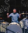 Drummer playing in front of 50 Pack High Density Acoustic Foam Panels 2x12x12 Inches Soundproof Wedges For Studio And Home Office.