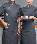 Men's Short Sleeve Chef Jacket Gray Breathable Kitchen Work Uniform Durable Restaurant Coat Sweat Wicking Culinary Staff Apparel Built Tough For The Daily Grind worn by two chefs in a kitchen setting.