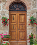 Wooden double door with Rustic Gate Handle Set 2 Pack Iron Hardware Pull With Screws Black Finish, surrounded by stone wall and flowers.
