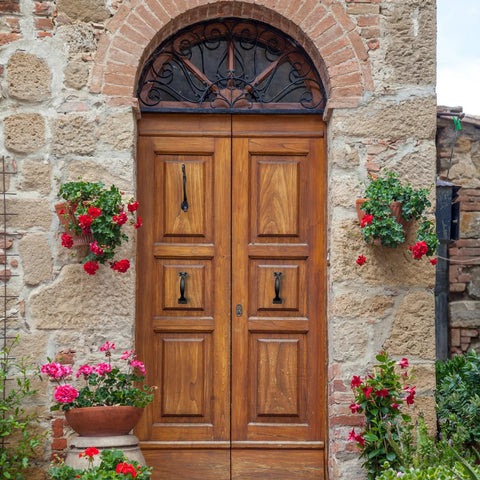 Wooden double door with Rustic Gate Handle Set 2 Pack Iron Hardware Pull With Screws Black Finish, surrounded by stone wall and flowers.