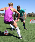 Two people playing soccer on grass with Portable Pop Up Soccer Goals For Backyard Set Of Two 4 Foot Nets visible in background