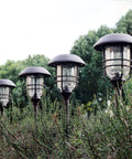 Lit Solar Path Lights 4 Pack Waterproof Metal Outdoor Lights with Glass and Stainless Steel Housings in a garden setting.