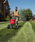 Person using Heavy Duty 50 Lb Broadcast Fertilizer Spreader For Lawns with adjustable drop rate in a residential garden.