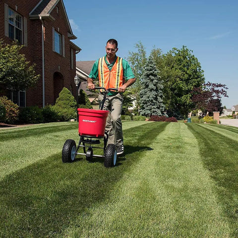Person using Heavy Duty 50 Lb Broadcast Fertilizer Spreader For Lawns with adjustable drop rate in a residential garden.