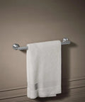 Composed 18 Inch Towel Bar In Polished Chrome, Tarnish Resistant, with white towel hanging, installed on a beige bathroom wall.