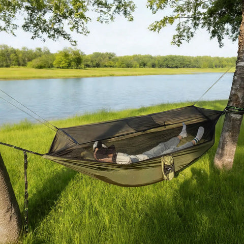 Person resting in Bug Free Camping Hammock With Mosquito Net, Ultralight Portable Outdoor Hammock, set up between trees near water.