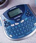 Portable Handheld Label Maker With QWERTY Keyboard And 2 Line Printing on a countertop displaying the word 'SUMATRA' on screen.