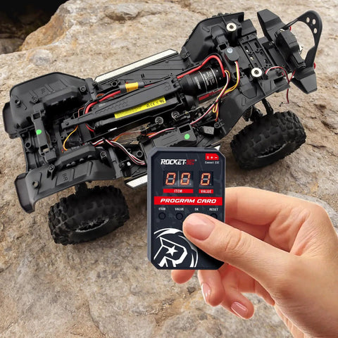 Hand holding RC Car ESC Programming Card With LED Programmer For 3660 Fusion Brushless Motors next to RC car chassis