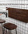 Folding Wall Desk With Solid Wood Board And Two Iron Brackets, 2.8cm Thick, shown folded on wall in cafe setting.