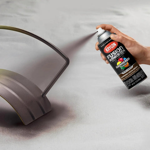 Person spraying Killer Hammered Finish Spray Paint In Deep Cocoa Brown on metal object, 12 oz aerosol can.