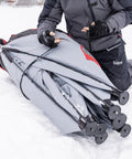 User preparing the Quickfish Six Person Portable Pop Up Ice Fishing Shelter With Fully Quilted Insulation No Trip Door And Deluxe Anchors For Hell Of A Winter Setup In Red Black on snow.