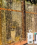 Battery Operated Fairy Curtain Lights With Remote Timer Nine Point Eight Feet By Nine Point Eight Feet Of Warm White LEDs For Bedroom Patio Wedding Backdrop Decor Easy To Install shown illuminating a window