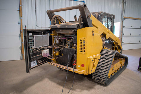 Construction vehicle under maintenance with engine compartment open, showcasing inner mechanics in a garage setting.
