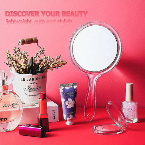 Double Sided Handheld Mirror With 1X And 2X Magnification Clear Handle Round Makeup Mirror For Face Detailing And Mascara Application Great For On The Go, shown with handle facing down on pink background among beauty products.
