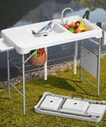 Outdoor setup of Beefy All Weather Folding Fish Cleaning Table With Dual Sinks, white, showing faucets and storage features