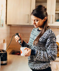 Person using corded electric milk frother with plug in handheld whisk in kitchen for coffee foam making.