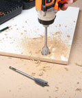 Front view of EnerTwist drill/driver drilling into plywood on a workbench; metal spade bit sits nearby.