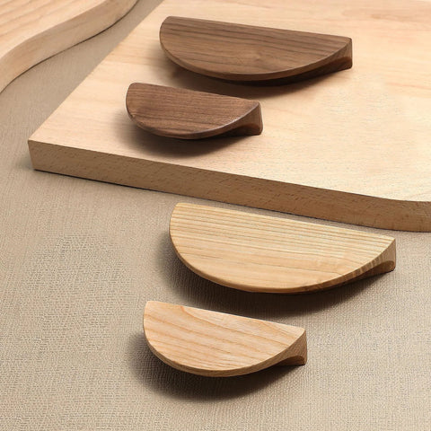 Variety of semi-circular wooden cabinet drawer pulls displayed on a textured surface, showing walnut and lighter wood finishes.