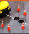 Six Pack 28 Inch Traffic Safety Cones With Reflective Collars arranged around open manhole near yellow vehicle on wet road