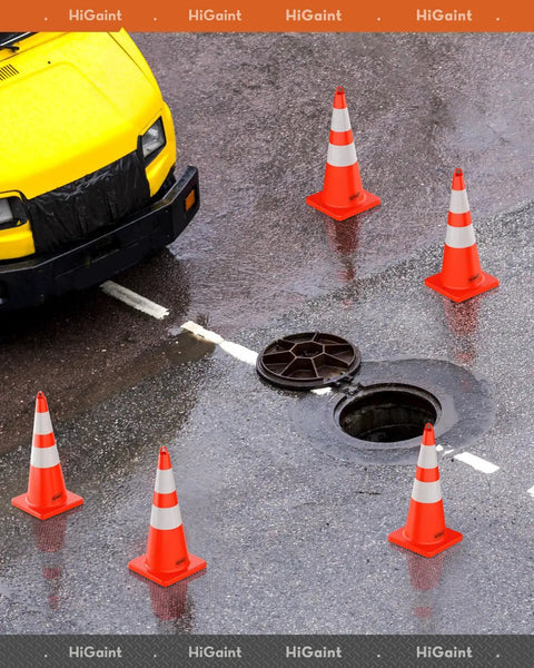 Six Pack 28 Inch Traffic Safety Cones With Reflective Collars arranged around open manhole near yellow vehicle on wet road