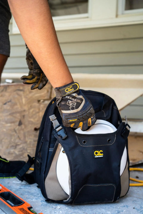 Person placing a hard hat into the Rugged Carpenter Tool Backpack With 44 Pockets And Padded Back Support For Comfort Dual Main Compartments
