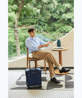 Man sitting with 14 Inch Underseat Carry On Luggage With Spinner Wheels And USB Charging Port on a cafe patio.