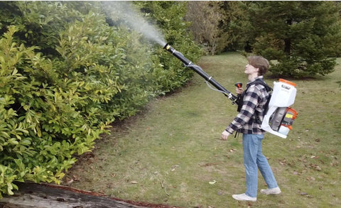 Person using Backpack Mosquito Fogger With Turbo Pump M915 Cold Fogger And Mister Duster spraying foliage in outdoor garden area.