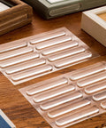 Clear Stick-On Cabinet Door Bumpers Pack Of 40 on a wooden table, showing silicone strips for quiet closings, 2.75x0.4 inches.
