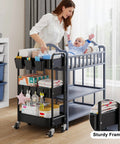 Three Tier Metal Rolling Cart On Wheels In Black, used as nursery organizer, beside crib, holding baby items and essentials.