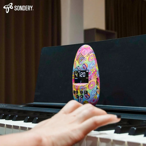Rechargeable Digital Metronome For Musicians With Color Screen And USB Headphone Jack in use on piano, vibrant design, A3 Art Series