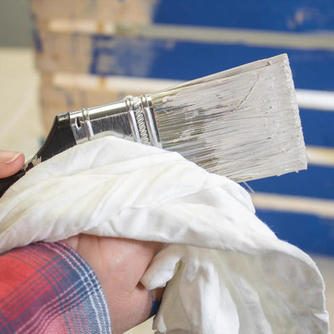 Hand holding paintbrush and Premium White T Shirt Cleaning Rags For Cleaning Staining Painting And More In A 2x25 Lb Compressed Box White Cotton Cloths For Spills Dust Oil Grease And Wood Finish Polishing Eco Friendly Reusable