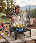 Person cooking on Heavy Duty Cast Iron Propane Burner With Adjustable Regulator Hose For Outdoor Camping And Wok Cooking Portable Gas Stove