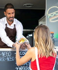 Man serving food to woman with Burger Neon Sign For Wall Decor 12x12 Inch LED Neon Light in background, cafe setting
