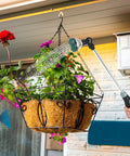 Person using 24 Inch Garden Hose Watering Wand With 8 Spray Patterns to water hanging basket of flowers on patio