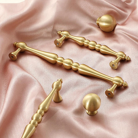 Two Pack 5 Inch Center Solid Brass Cabinet Pulls In Vintage Gold Brushed Finish on pink fabric background