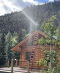 Log cabin with activated Wildfire Protection Sprinkler System With Bracket And Hardware, spraying water, forest backdrop.