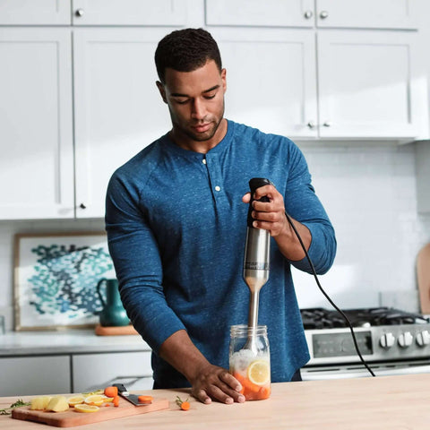 Hella Powerful Immersion Blender With Five Speed Settings And A 625-Watt Motor That Handles Whole Foods And Creates Creamy Soups Smoothies And Baby Food In Sleek Stainless Steel Finish in use blending a jar of vegetables.